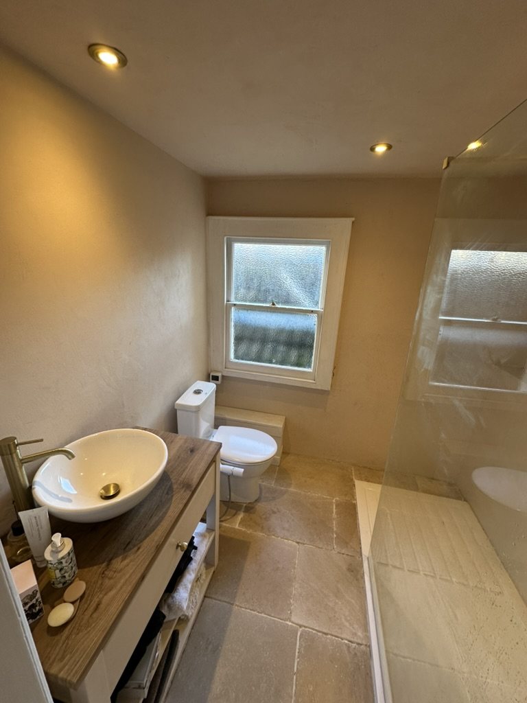 Finished bathroom from the door: basin on timber vanity, stone floor, shower beyond