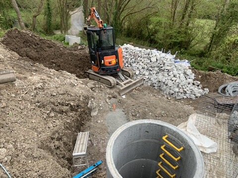 Precast chamber ring set in the ground beside a mini digger